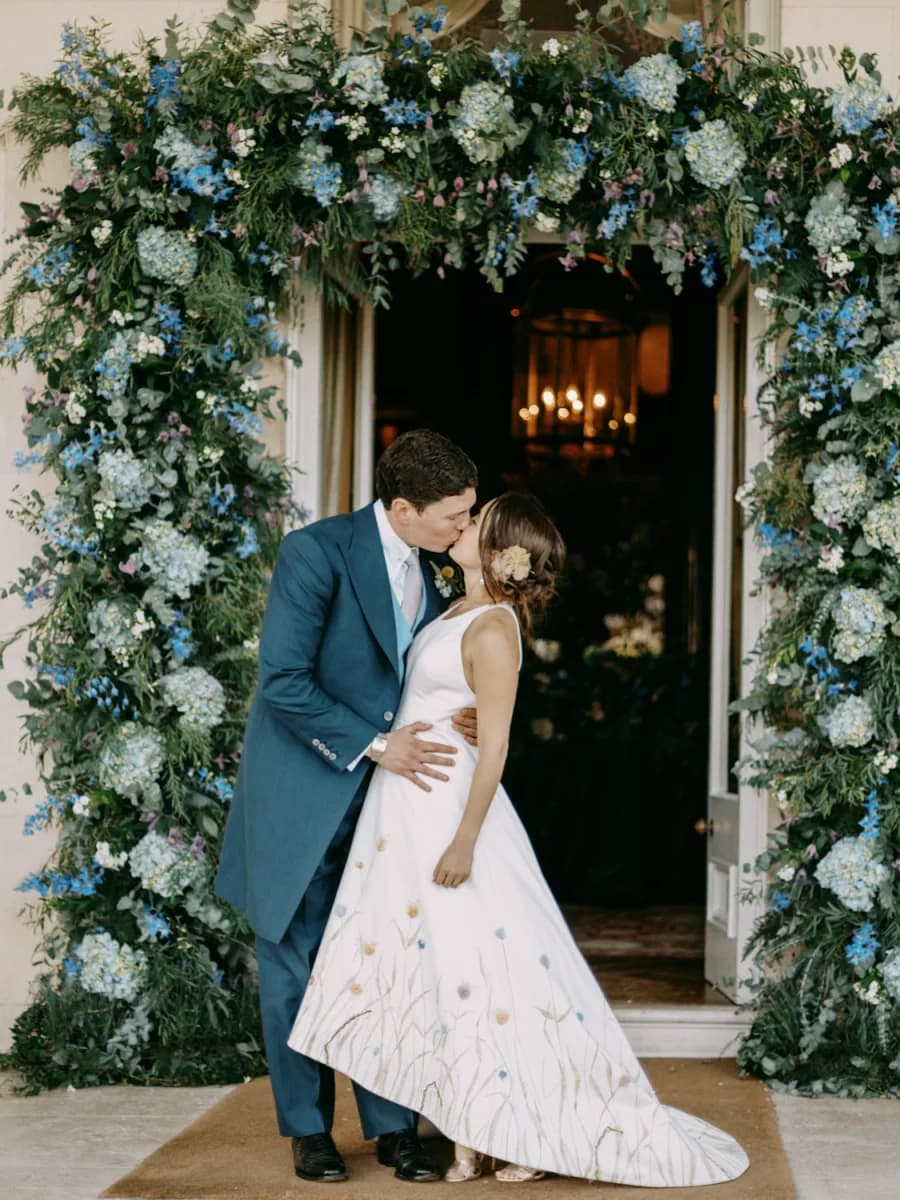 Newlyweds kissing beneath a floral arch at Goodwood House